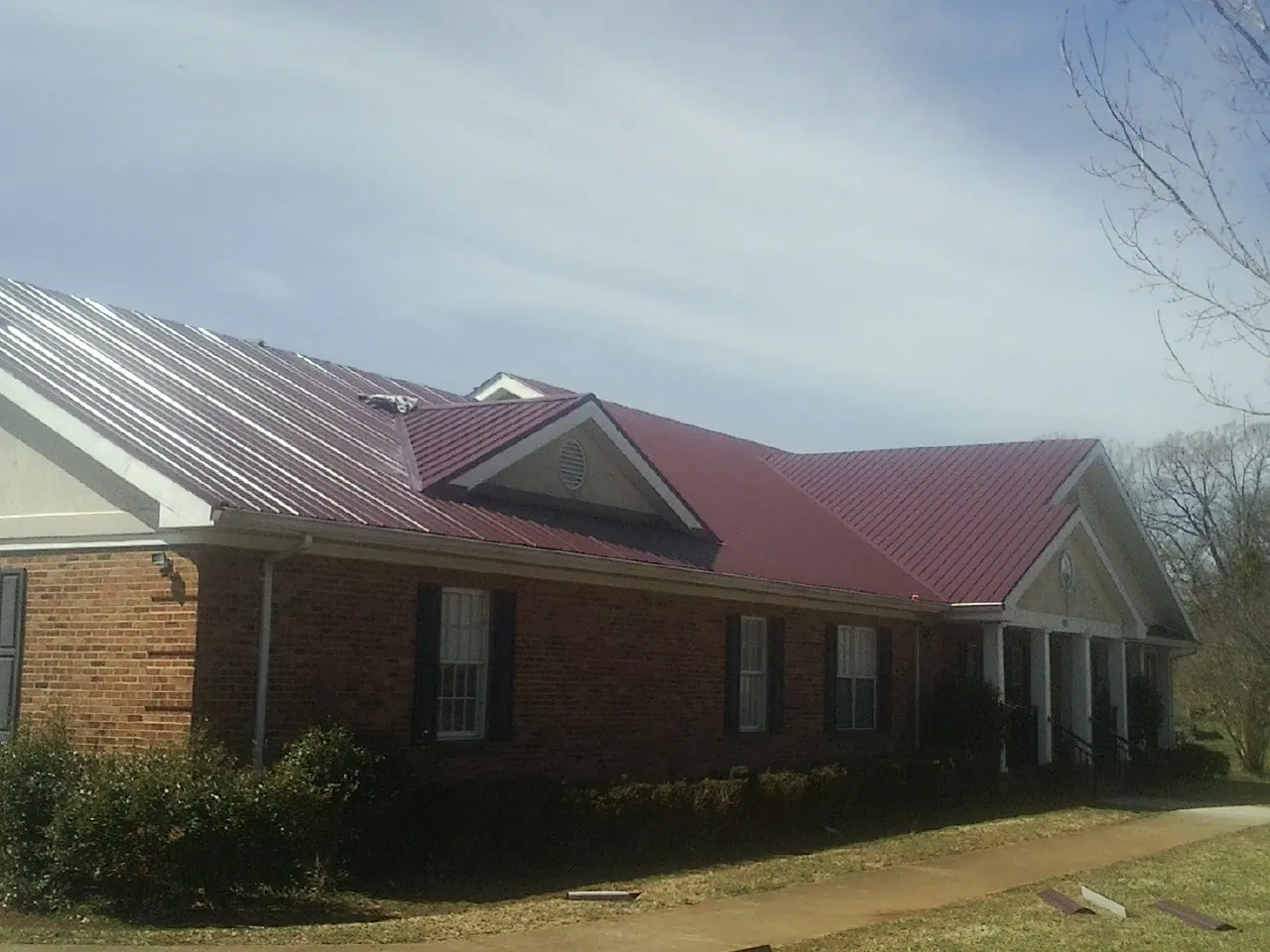 Red metal roof with gabled entries on a long brick building, from a Hail Damage Roof Repair job in Sultan