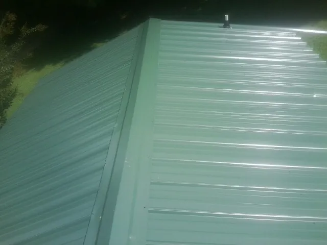 New green metal panels meeting at the ridge of a roof — Flat Roof Repair work by our crew in Sultan