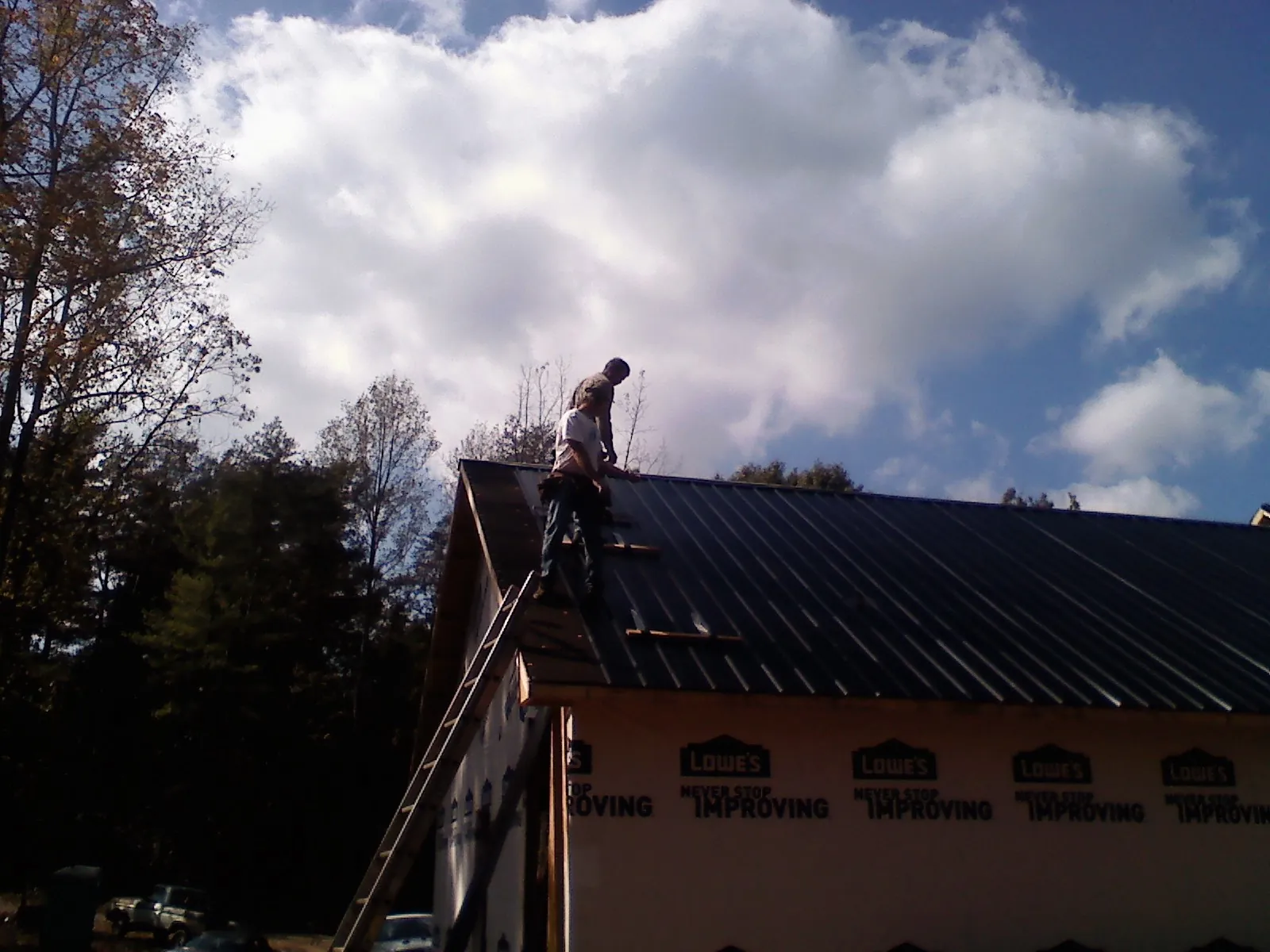 Roofer fastening dark metal panels high against a cloudy sky, from a Roof Inspection job in Sultan